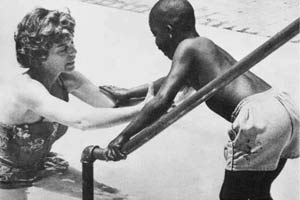 Mrs. Shriver gently guides a child into the pool for a swimming lesson